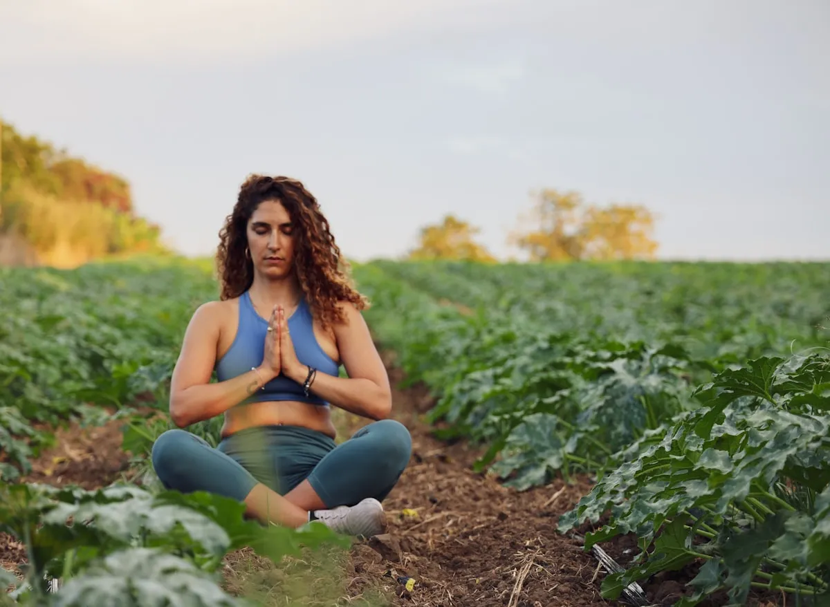 Woman meditating peacefully in a green field surrounded by nature